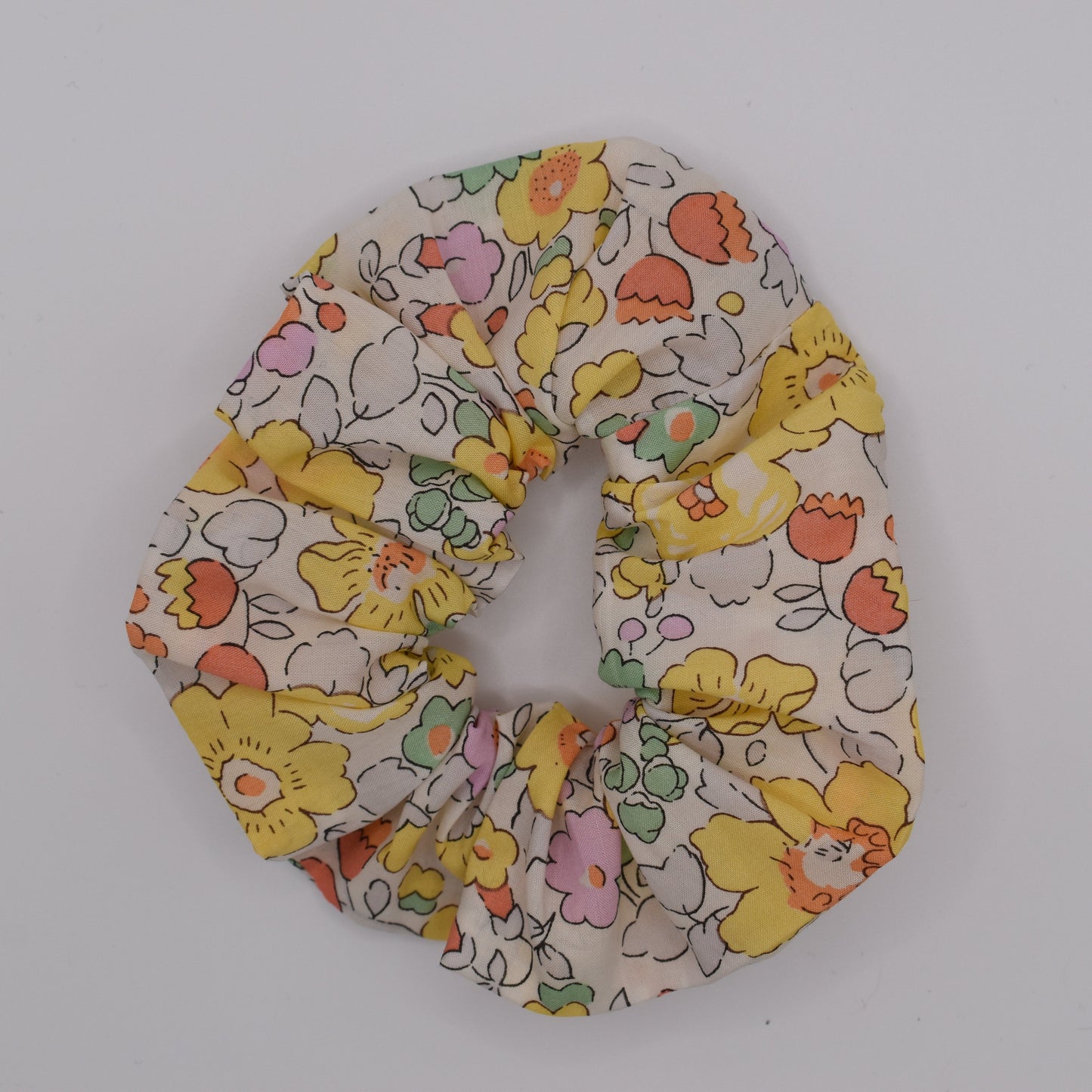 A Liberty hair scrunchie for girls using Betsy Yellow fabric. Made by The Blossom Tree House. Top down view