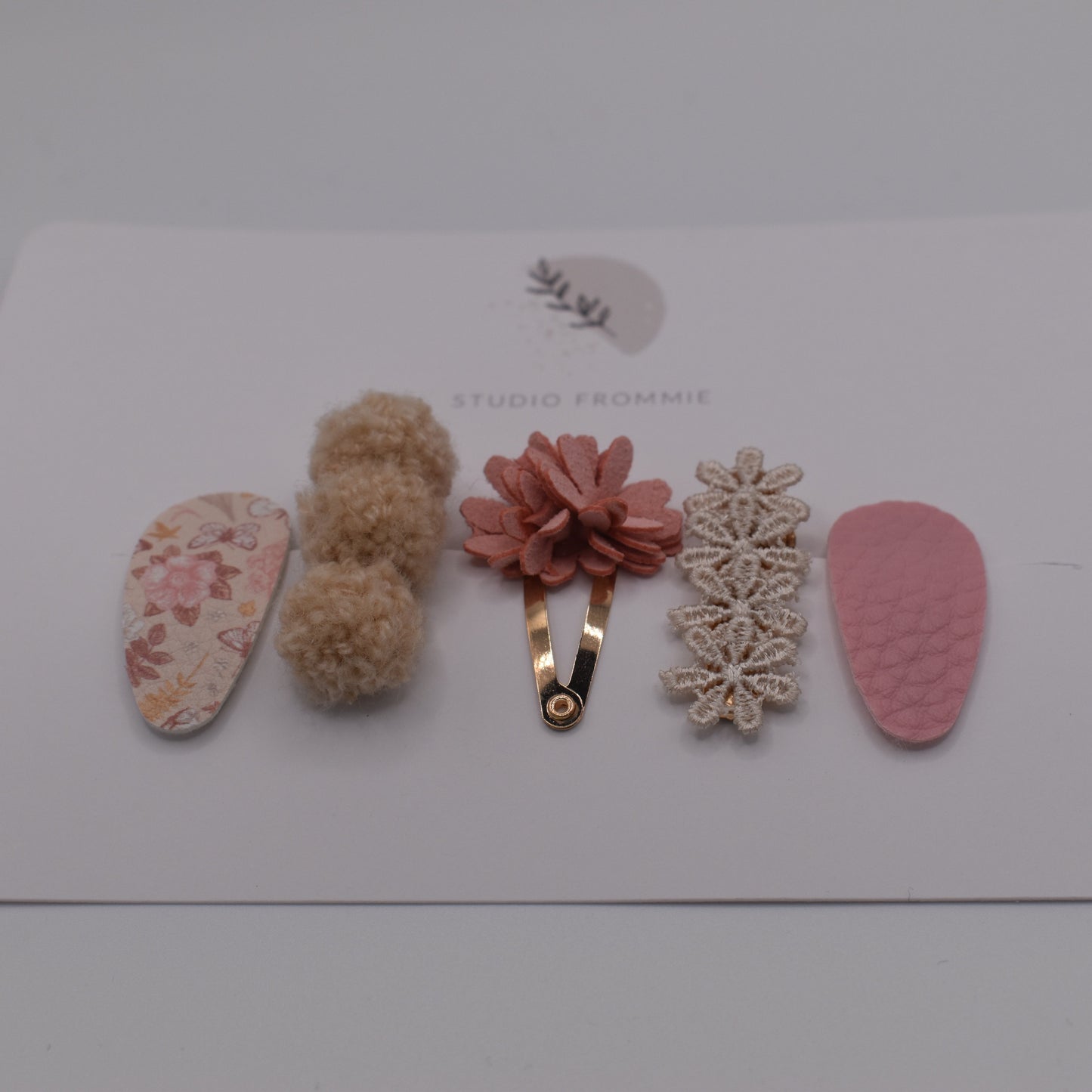 A mixed set of flower and pompom hair clips for girls. Pink and beige colours. Front view. Made by Studio Frommie