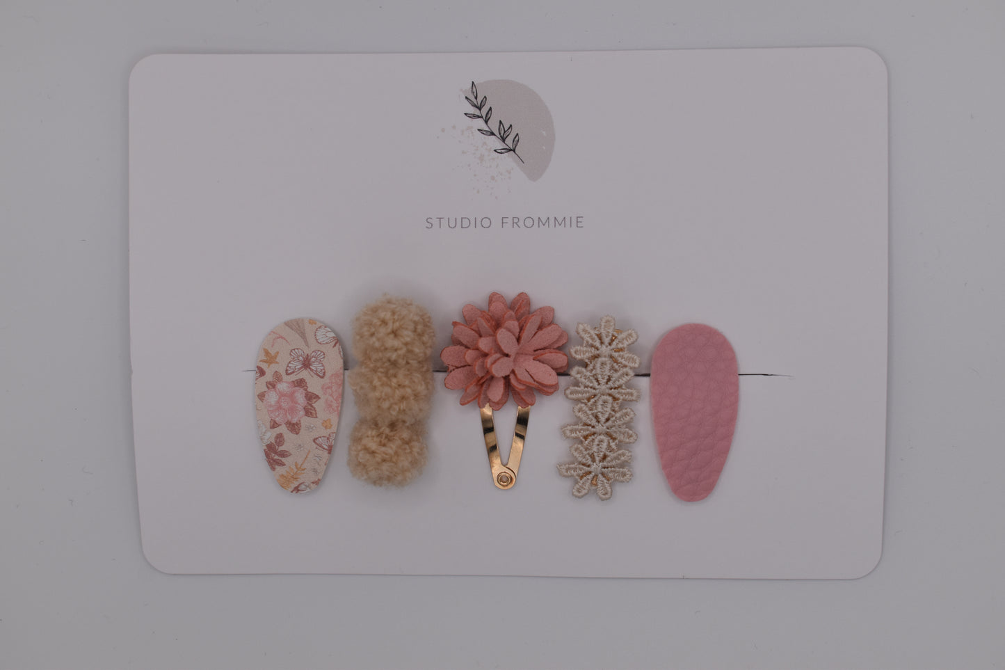 A mixed set of flower and pompom hair clips for girls. Pink and beige colours. Top view. Made by Studio Frommie
