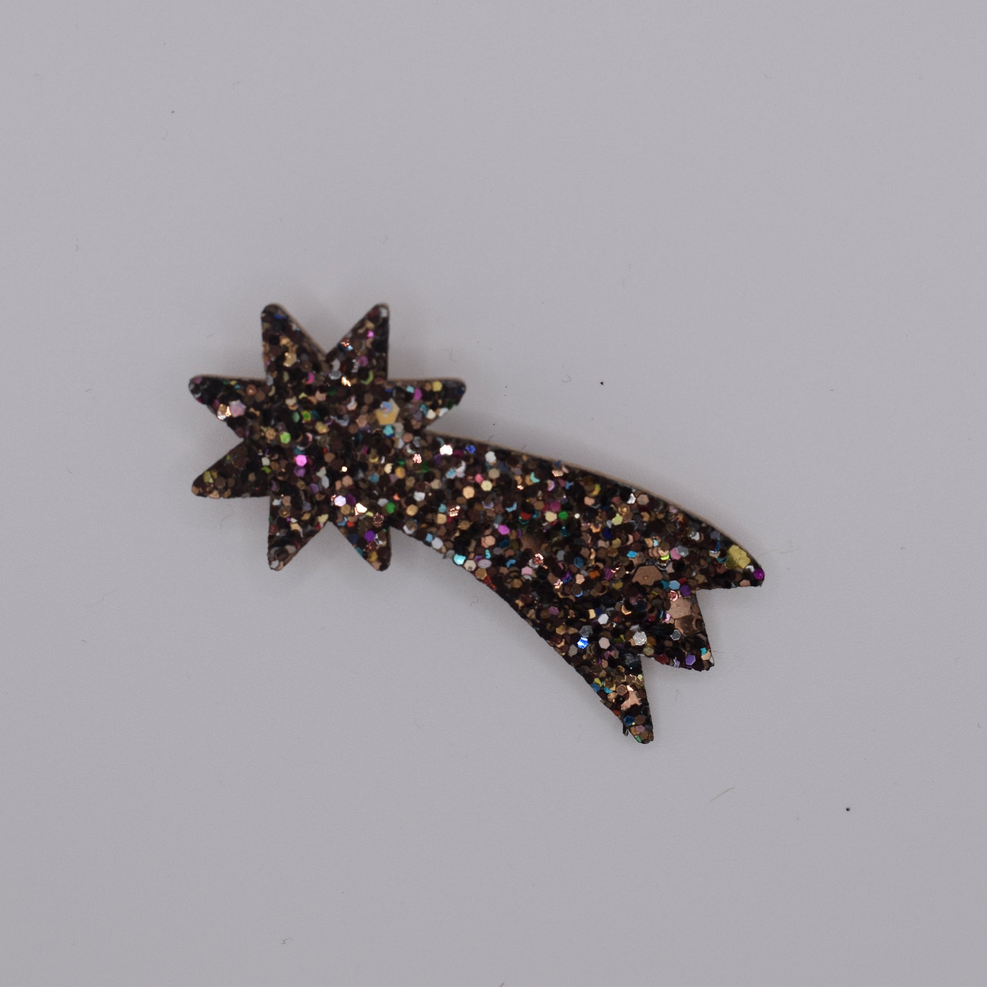 A shooting star bronze hair brooch for girls. Glittery. Top view with no backing card. Made by Luciole et Petit Pois