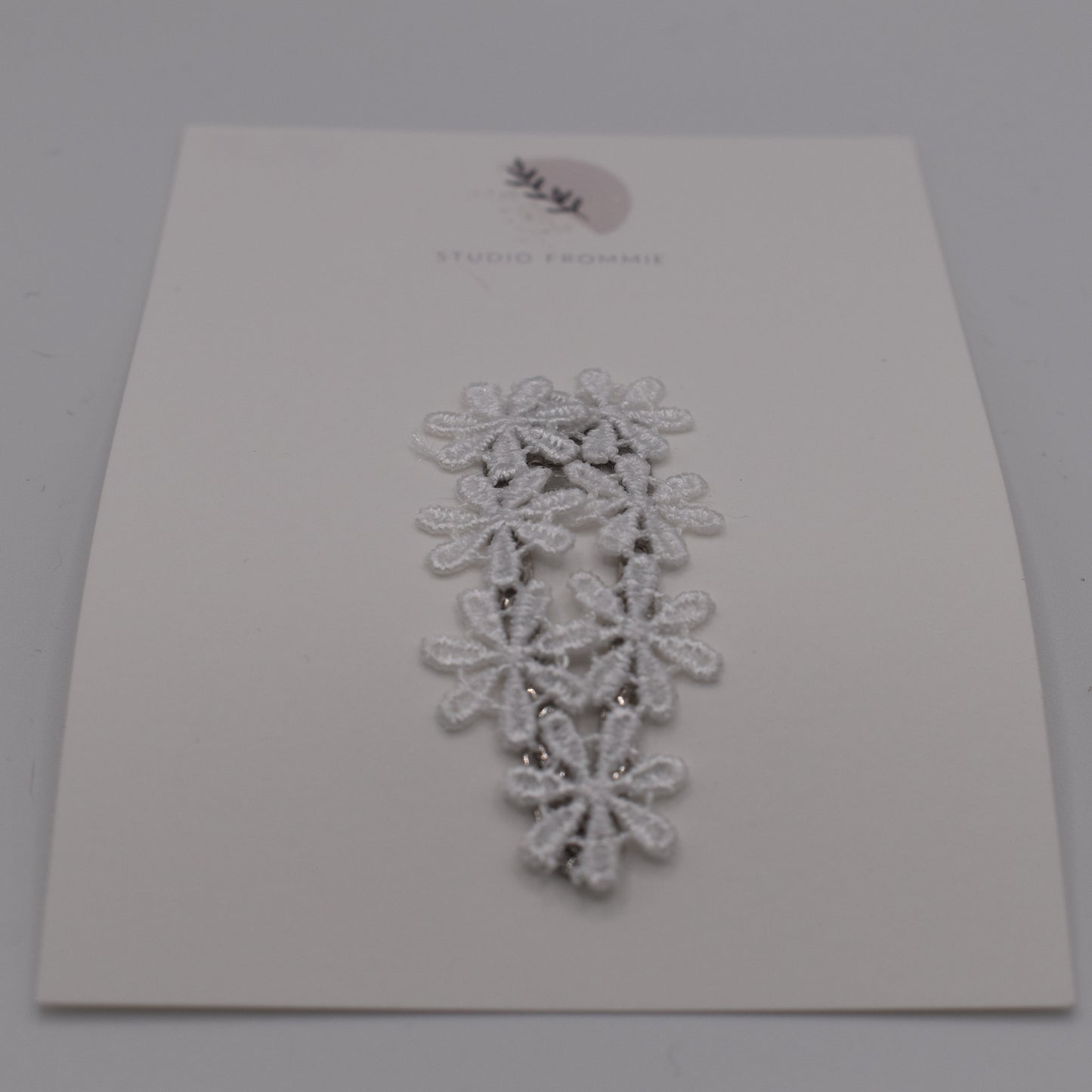 A daisy chain hair clip for girls. White fabric. Front view. Made by Studio Frommie