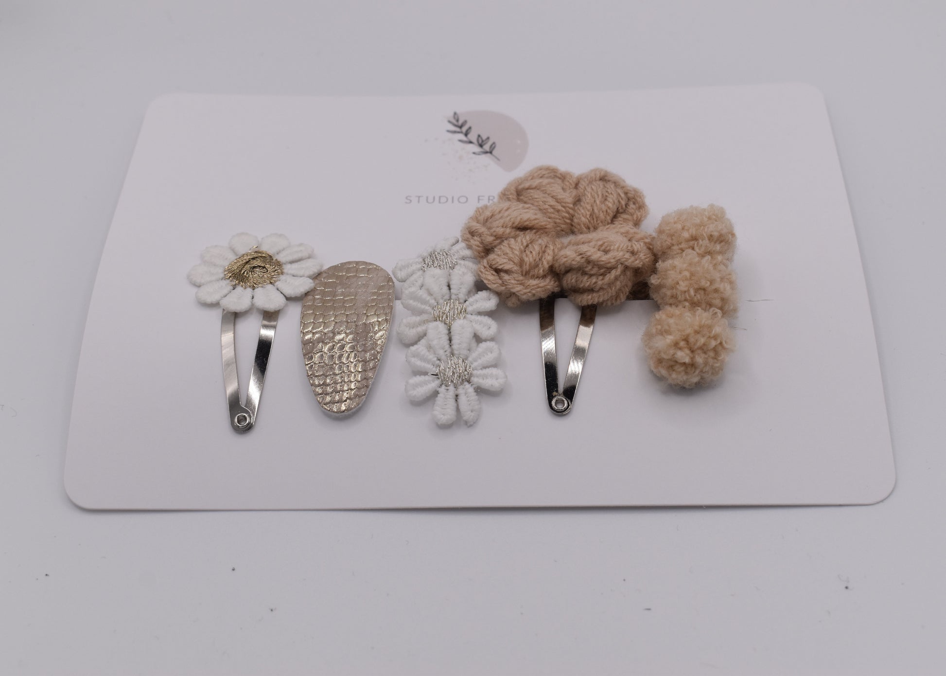 A flower and pompom hair clip set for girls. Beige and white colours. Front view. Made by Studio Frommie