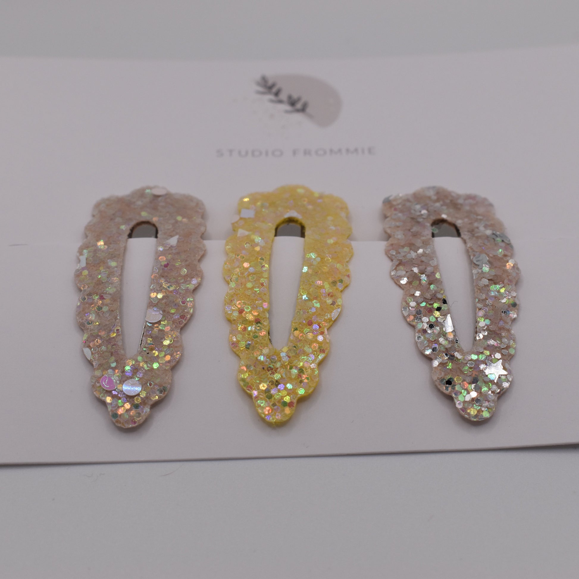 A set of glitter barrette clips for girls by Studio Frommie. Yellow and silver colours. Front view
