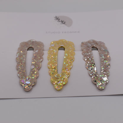 A set of glitter barrette clips for girls by Studio Frommie. Yellow and silver colours. Front view