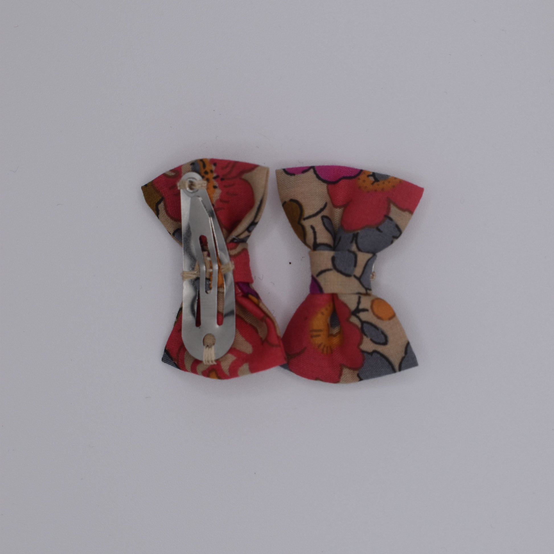 A pair of mini liberty bow hair clips for girls in Betsy Fluo Tea pattern. Back view with no backing card. Made by Luciole et Petit Pois