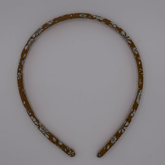 A girl's liberty print headband in Mustard Capel. Top-down view. Made by The Blossom Tree House