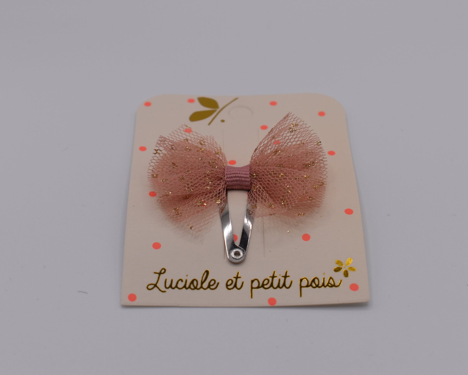 A mini tutu bow hair clip for girls. Pink fabric with gold sparkles. Front view. Made by Luciole et Petit Pois