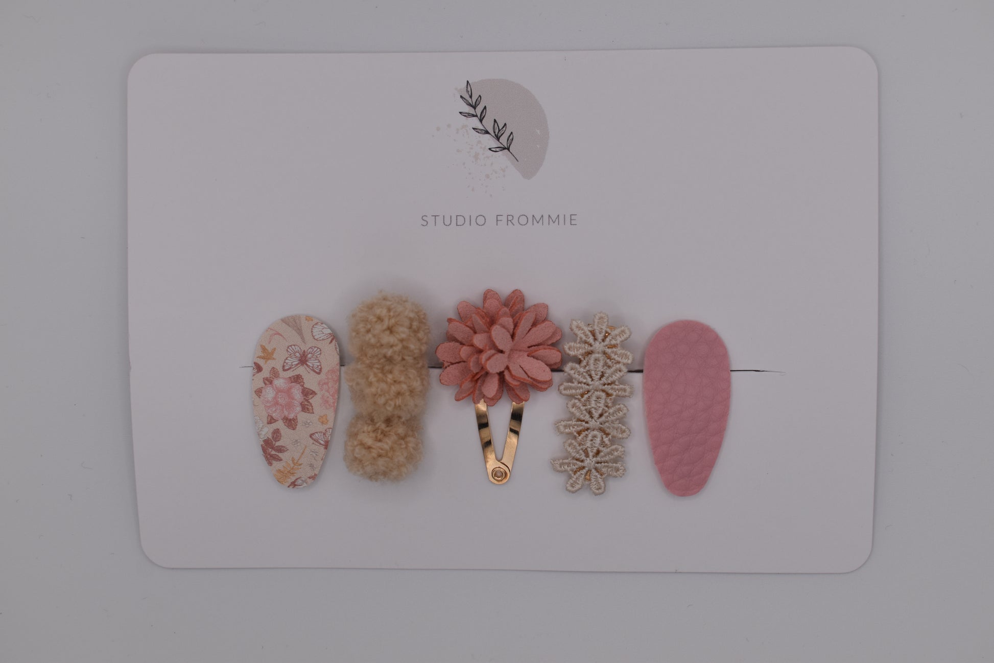 A mixed set of flower and pompom hair clips for girls. Pink and beige colours. Top view. Made by Studio Frommie