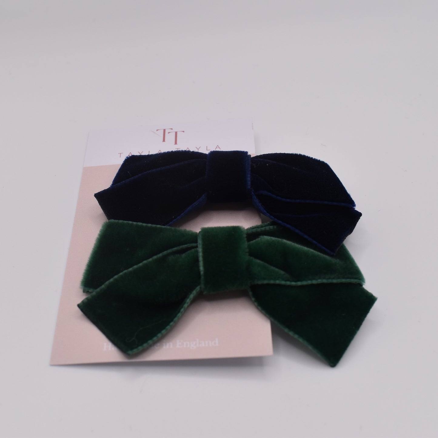 A pair of velvet hair bow clips for girls. One in navy and one in green. Front view. By Tayla Tayla