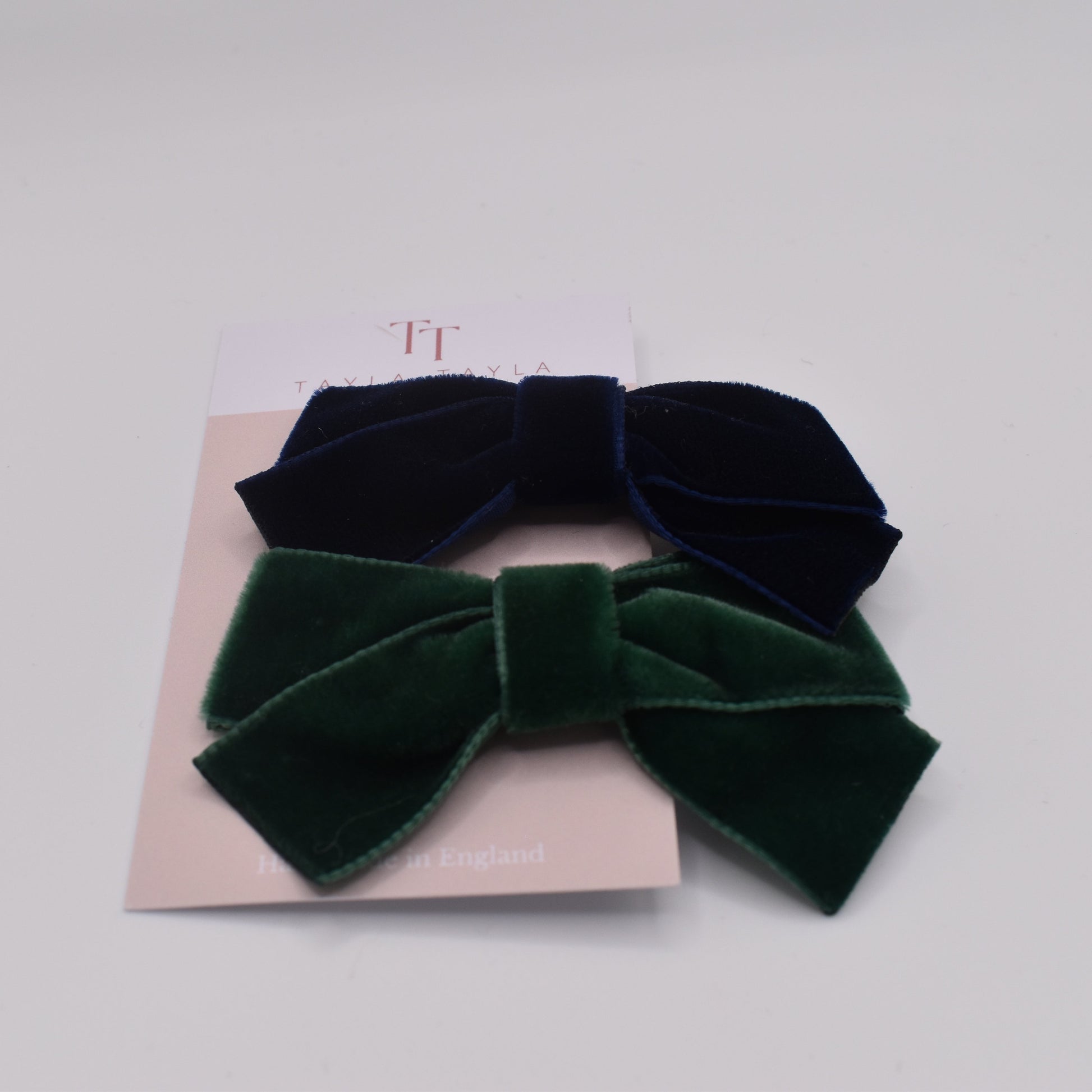 A pair of velvet hair bow clips for girls. One in navy and one in green. Front view. By Tayla Tayla
