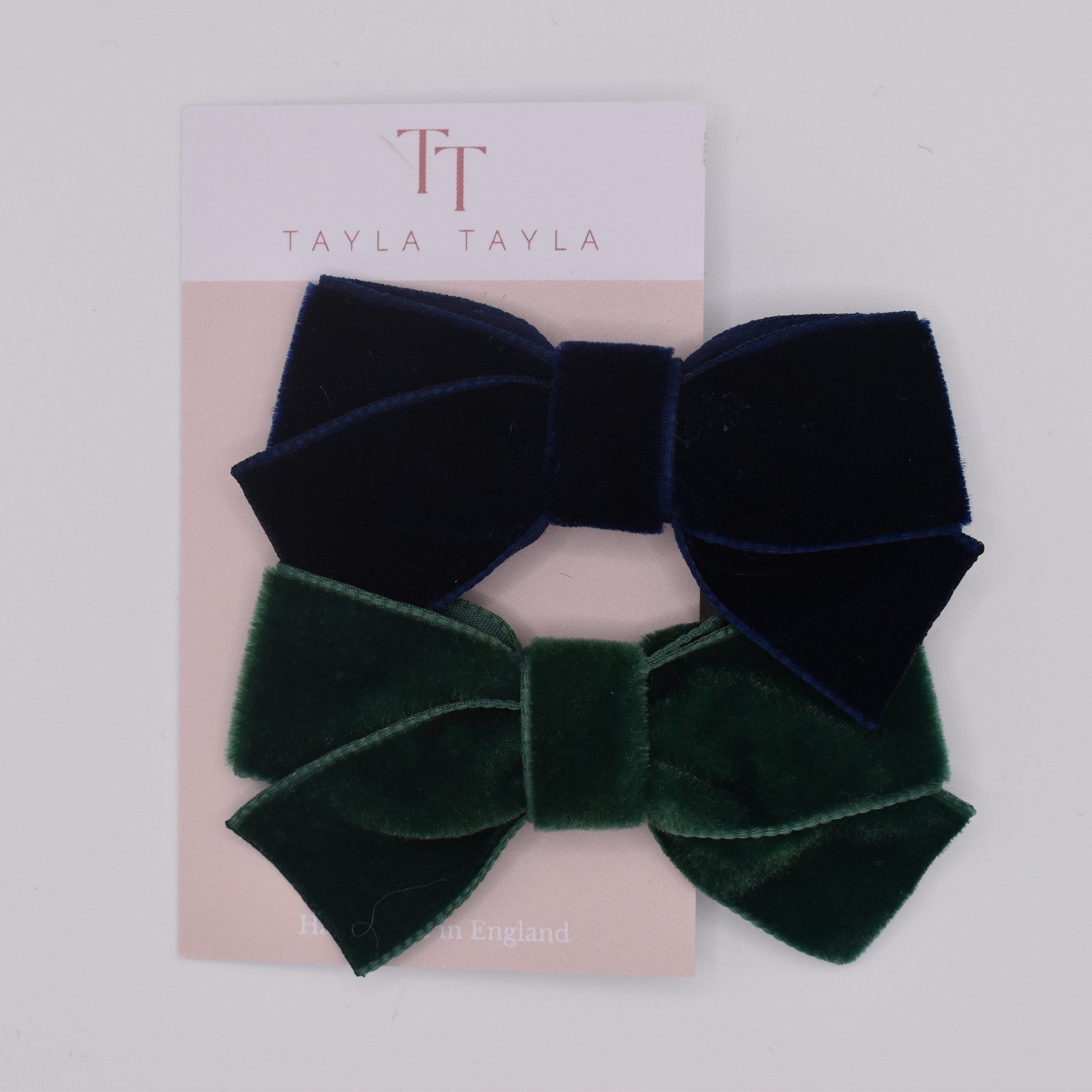 A pair of velvet hair bow clips for girls. One in navy and one in green. Top view. Made by Tayla Tayla