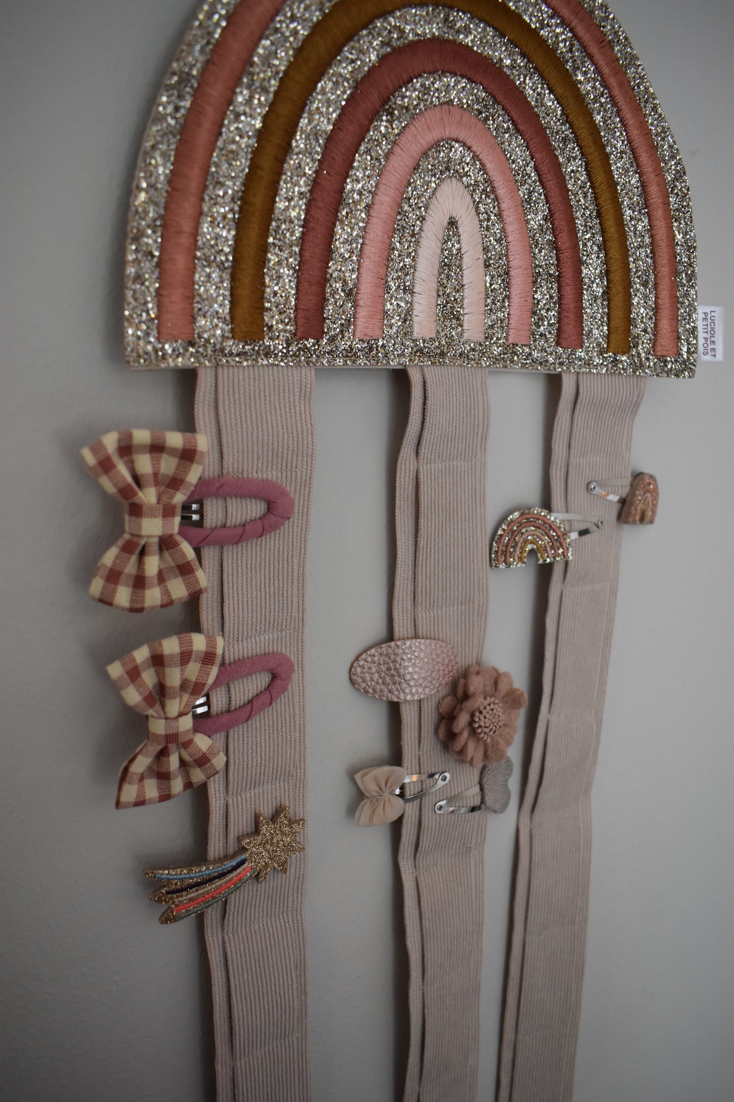 A rainbow hair clip holder. Glittery and wall hanging. Perfect for storage of girls hair clips. Angled view and in use with clips