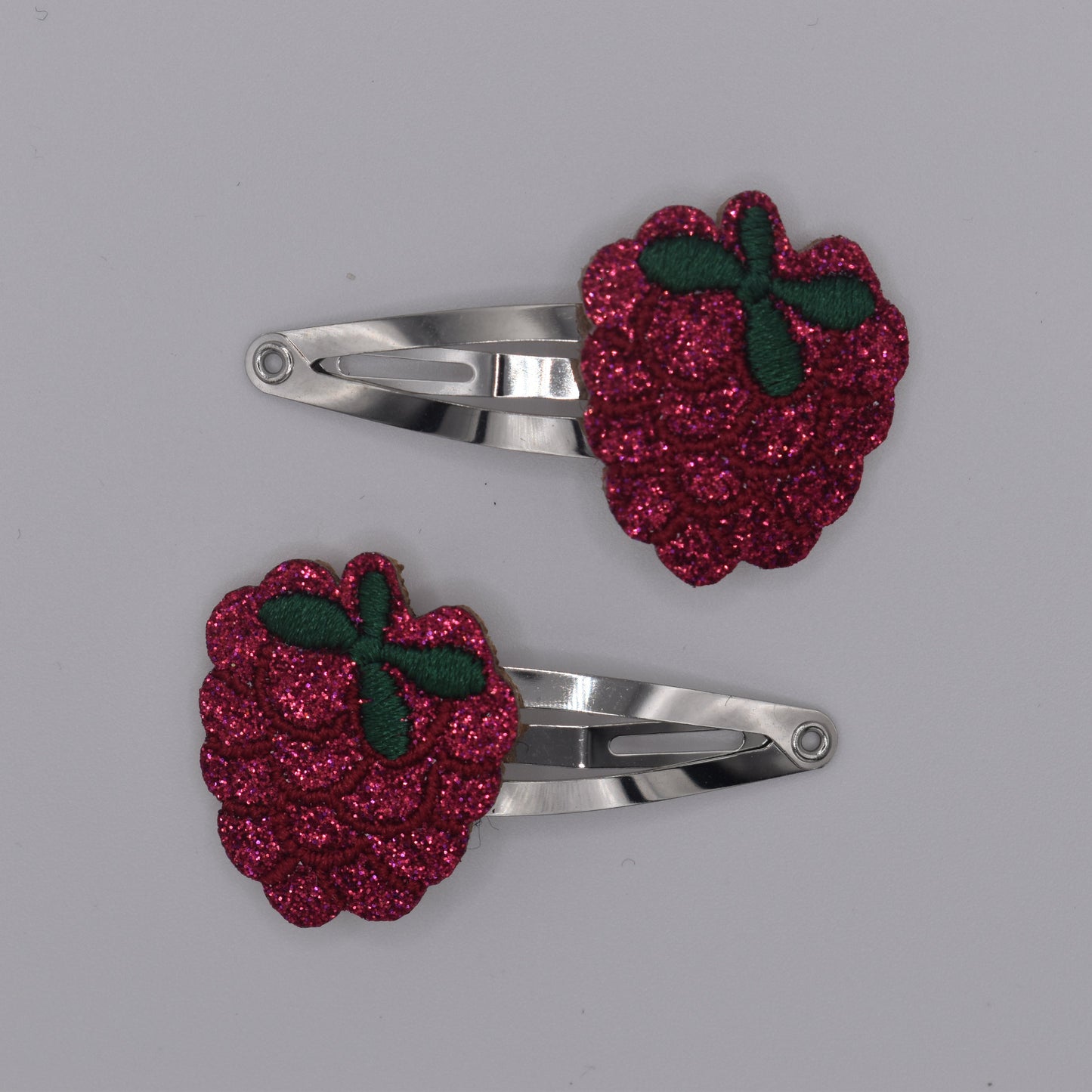 A pair of glitter raspberry hair clips for girls. Red colour. Top view with no backing card. Made by Luciole et Petit Pois