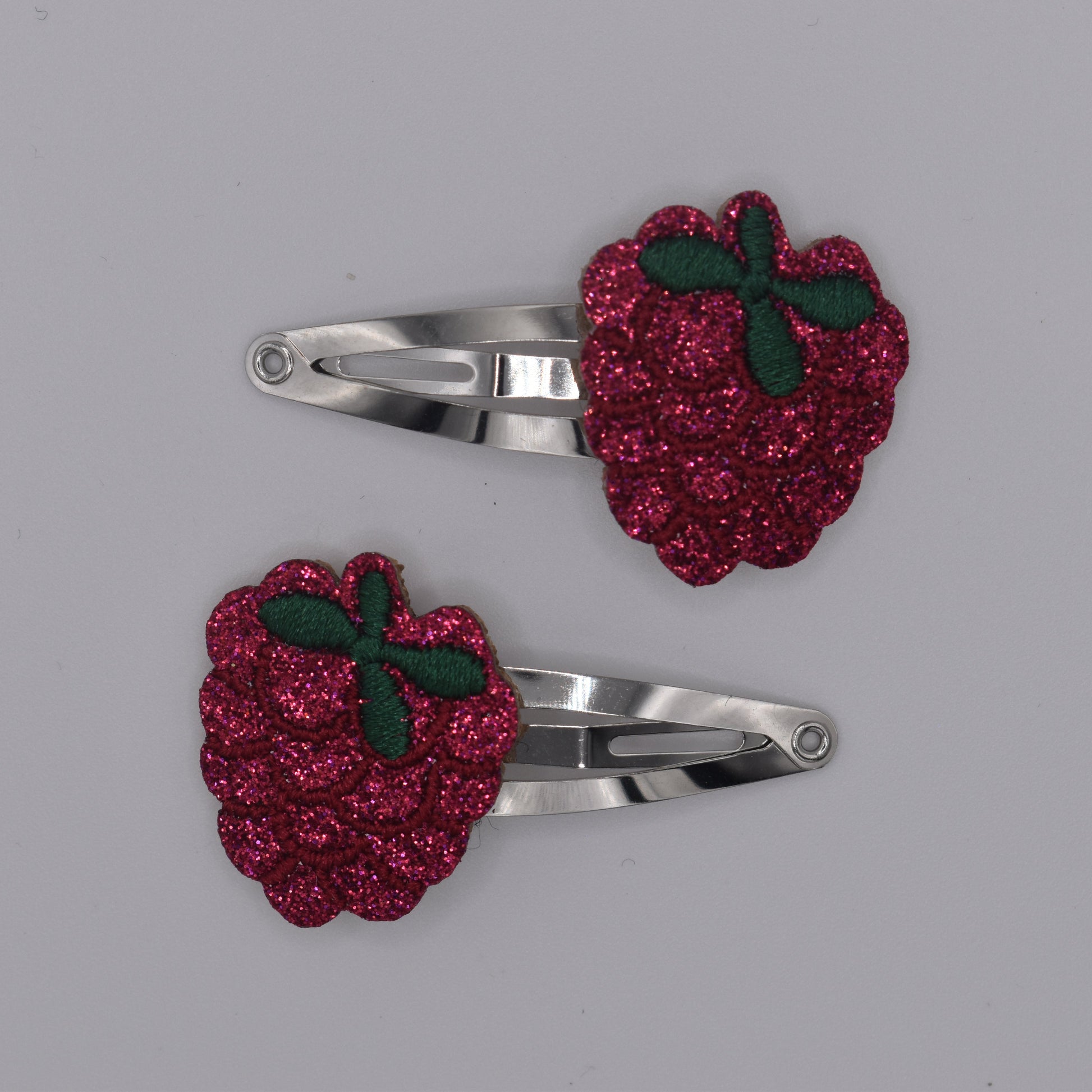 A pair of glitter raspberry hair clips for girls. Red colour. Top view with no backing card. Made by Luciole et Petit Pois
